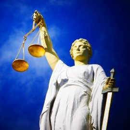 Eine Justizia-Figur hält eine Waage vor tief blauem Himmel
