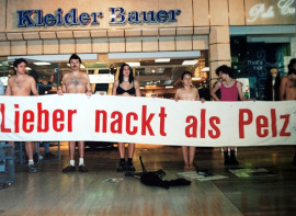 Spärlich bekleidete Aktivist:innen posieren mit einem großen Banner vor einer Kleider Bauer Filiale